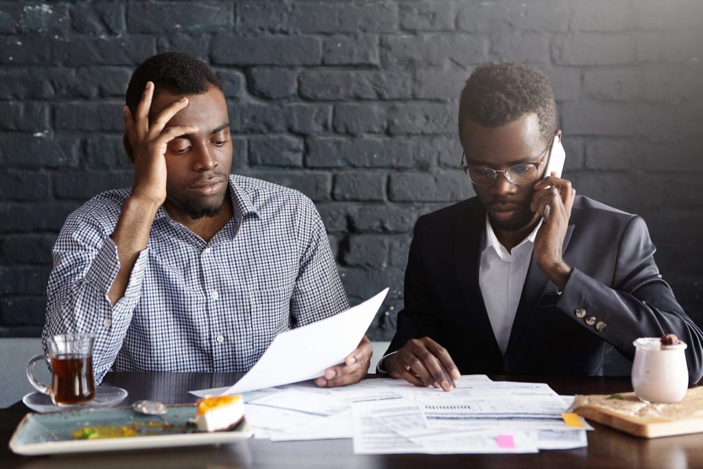 candid shot serious afro american colleagues formal wear working together office man shirt looking through papers while male wearing glasses having phone conversation looking worried 1 scaled